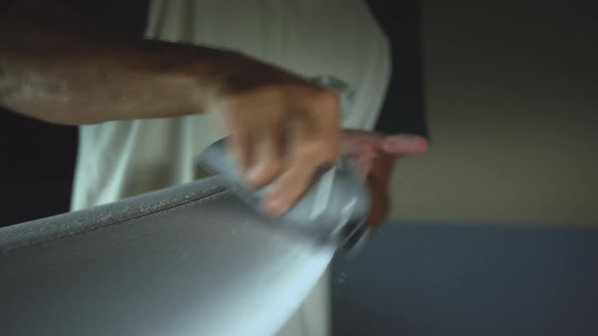 Male carving the edges of a surfboard