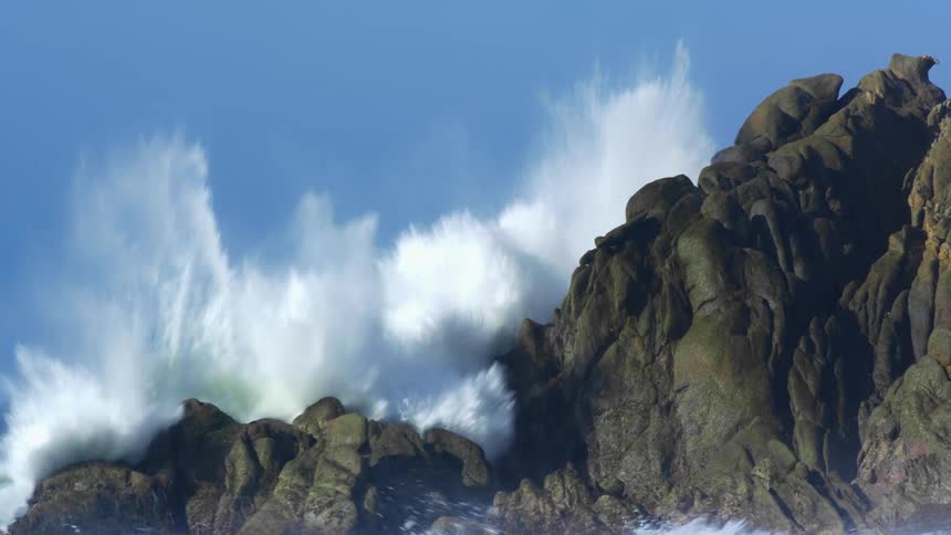 Ocean waves splash against rocks on a clear day