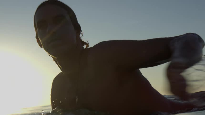 A man lies down and paddles on his surfboard in the ocean far from the beach