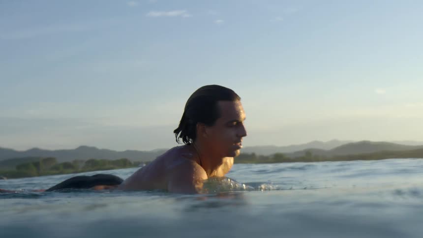 Male surfer paddles on the surfboard in the sea water