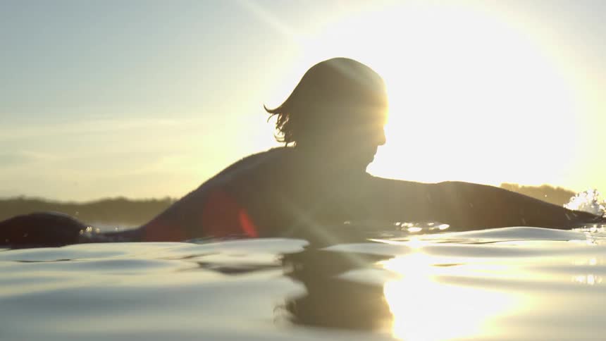 A surfer paddling on surfboard in the ocean at dawn