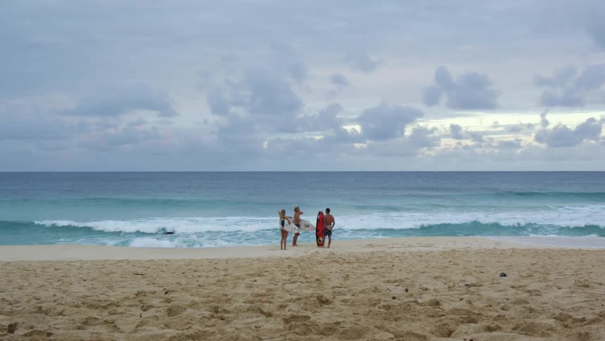 Three people standing on the beach at sunset next to the ocean