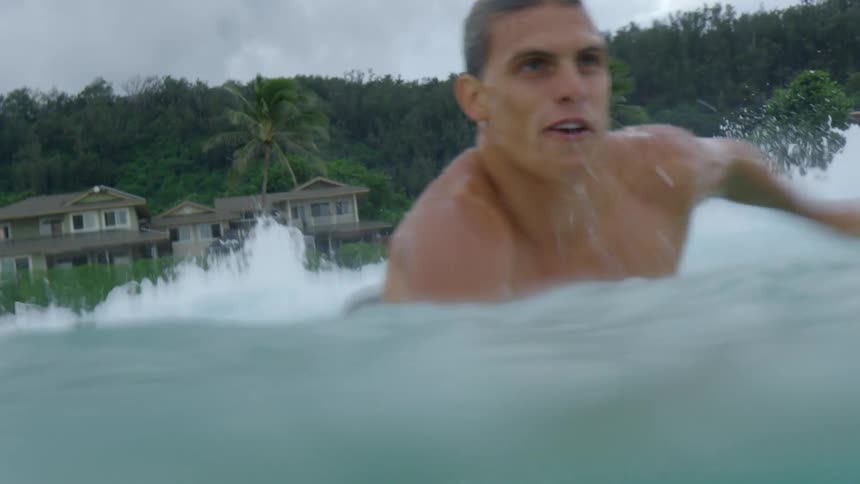 Male surfer paddles on the surfboard in the water