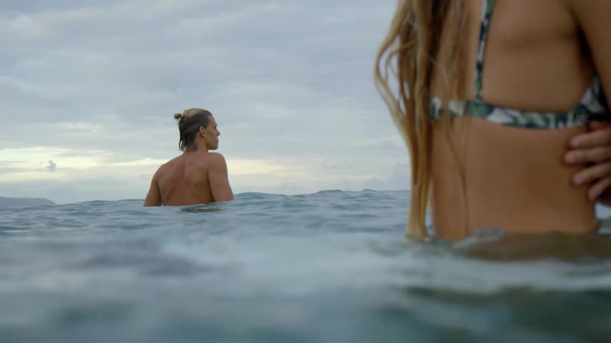 Two fit young people standing on the sea looking at the horizon at sunset