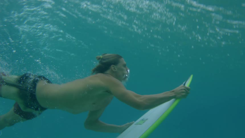 A man under water with his surf board rises to the surface