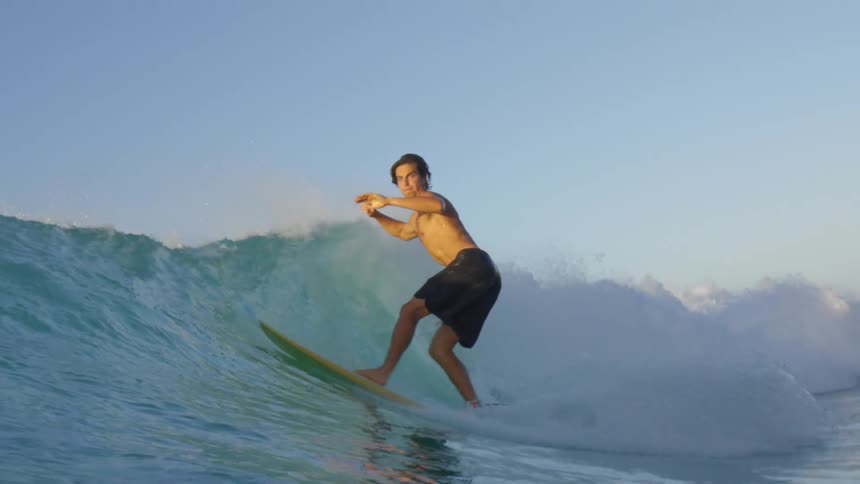 Male surfer with swimming shorts and a yellow surfboard rides a wave
