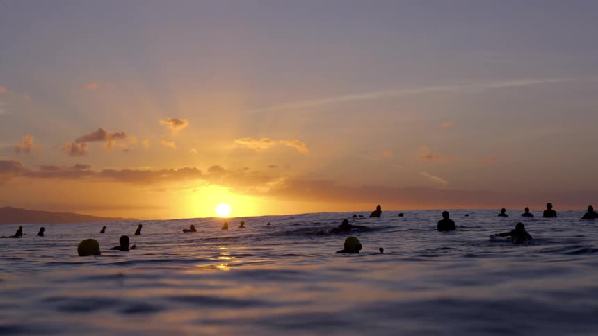 A crowd of people is silhouetted against the sunset in the sea