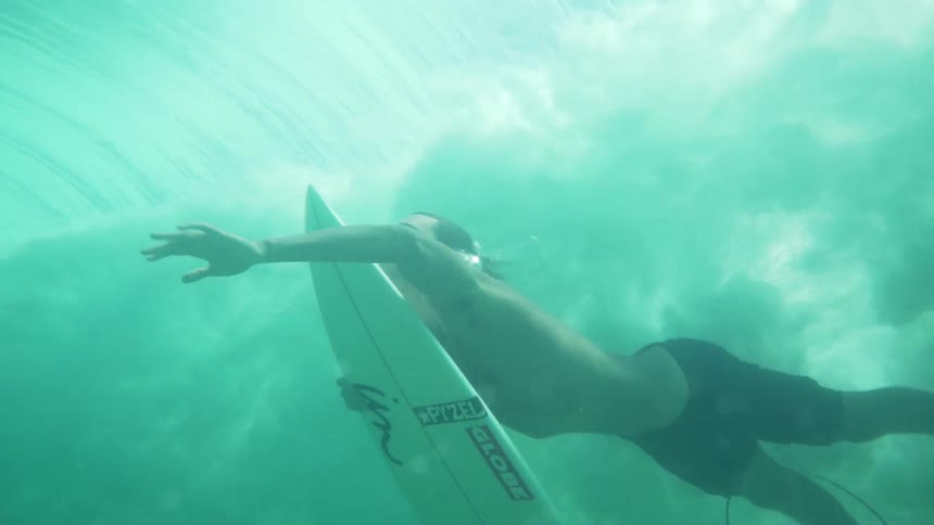 A surfer swimming beneath water as ocean waves crash down