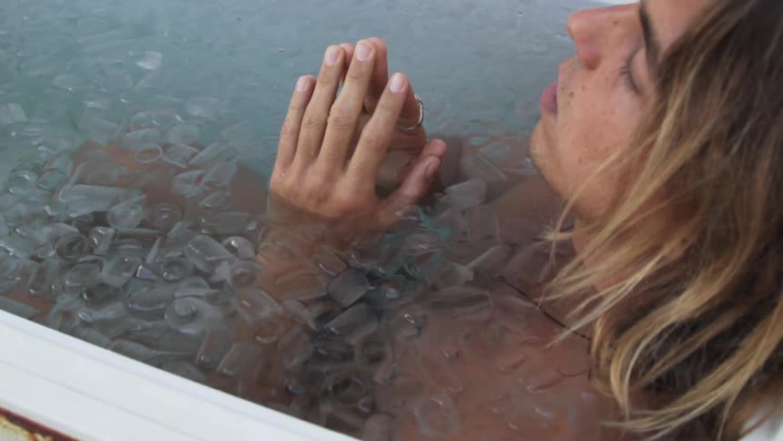 Man sits in rusty white tub of ice with hands templed together and eyes closed