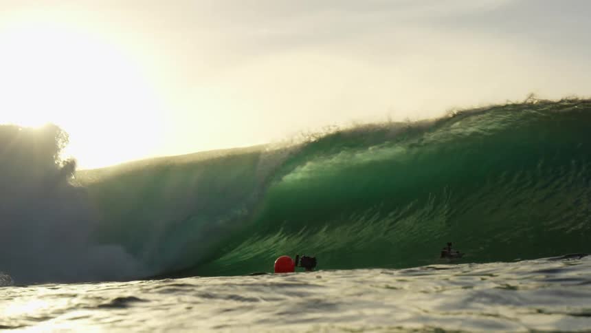 Big wave breaks against the beach at sunset