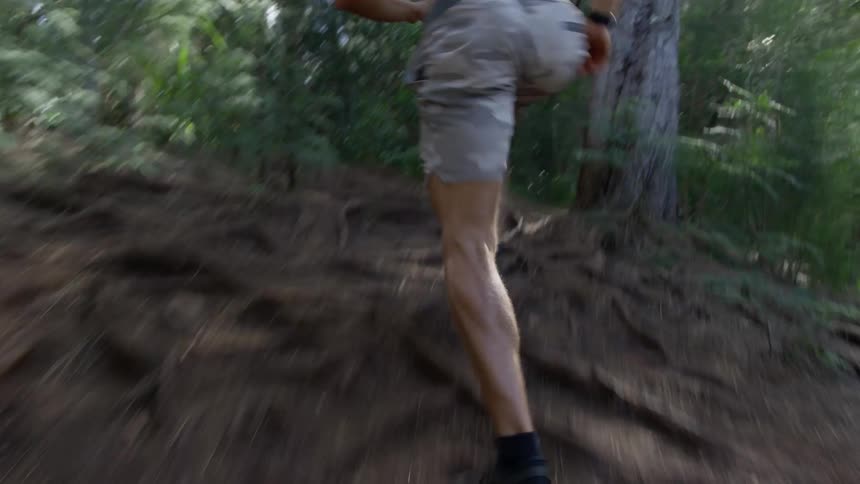 Man with shorts and and black shoes runs uphill in the woods