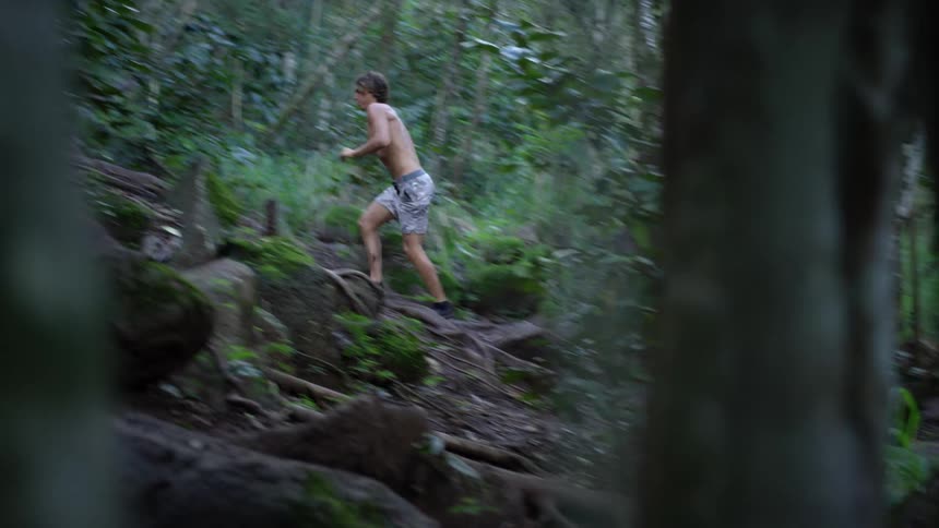 Shirtless man running uphill through a forest
