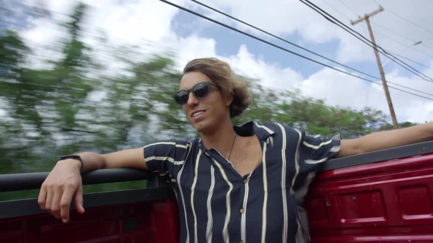 A man sits in the back of a truck that is driving down a road during the day