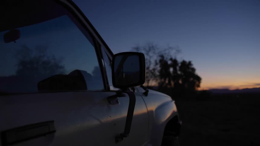 A vehicle is parked outdoors at sunset with a focus on the passenger side mirror