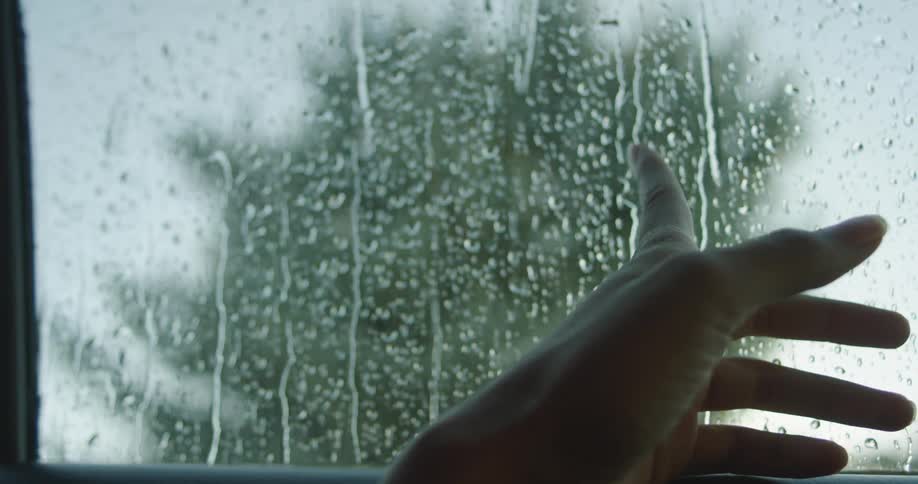 A woman runs her finger on a car window as the rain falls outside