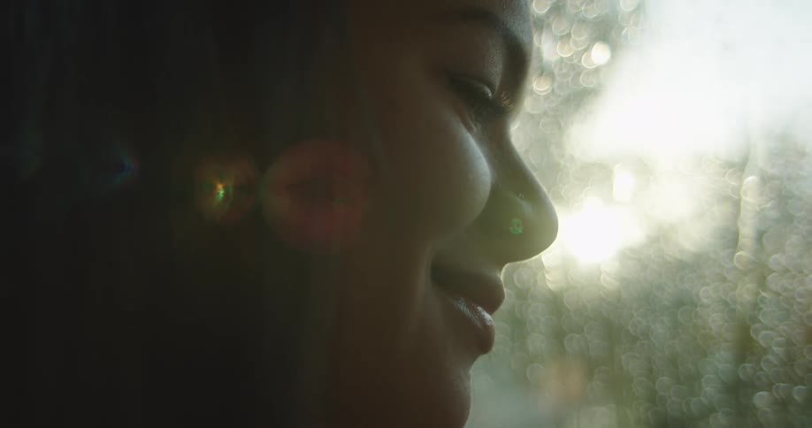 A woman smiles next to a window with rain falling down outside
