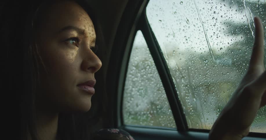 A woman is sitting in a car while its raining outdoors