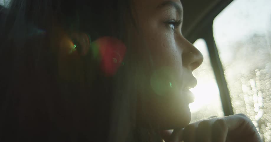 Young woman looking out the window of a car on the rain at sunset