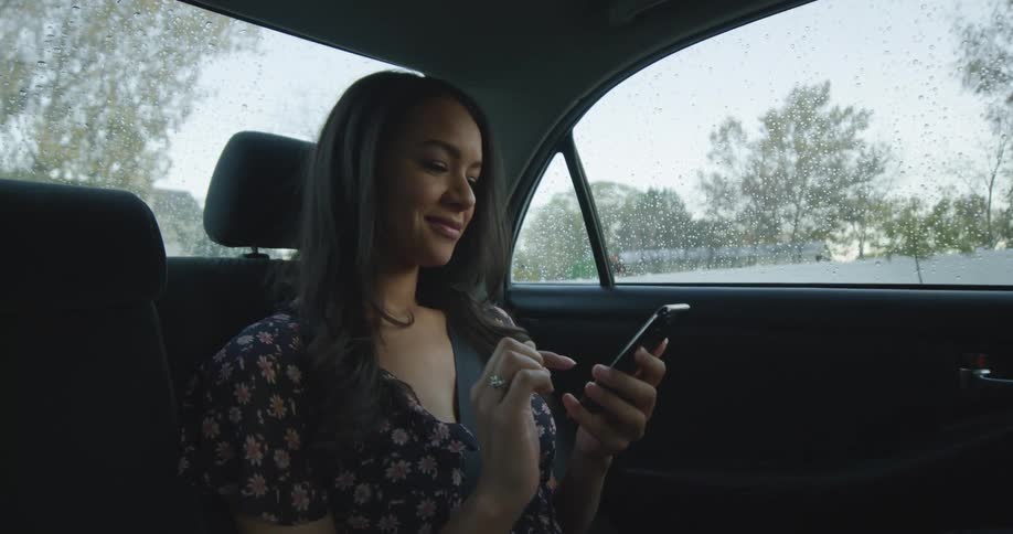 Young woman checks her phone and smile inside a car driving on the neighborhood