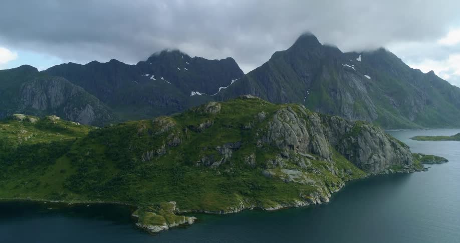 An aerial view of a body of water with mountains and green hills with an overcast sky at daytime