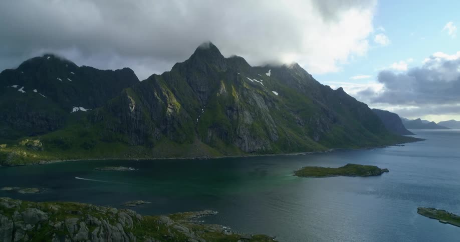 An aerial view of mountains and a body of water with rain clouds on one side of the sky with sunlight on the opposite