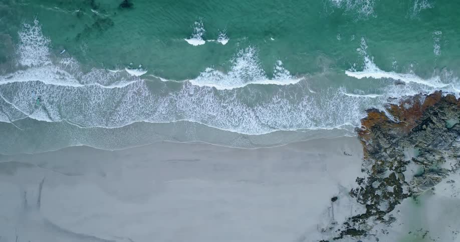 Aerial top down view of the ocean waves crashing on the rocks and sand of a beach