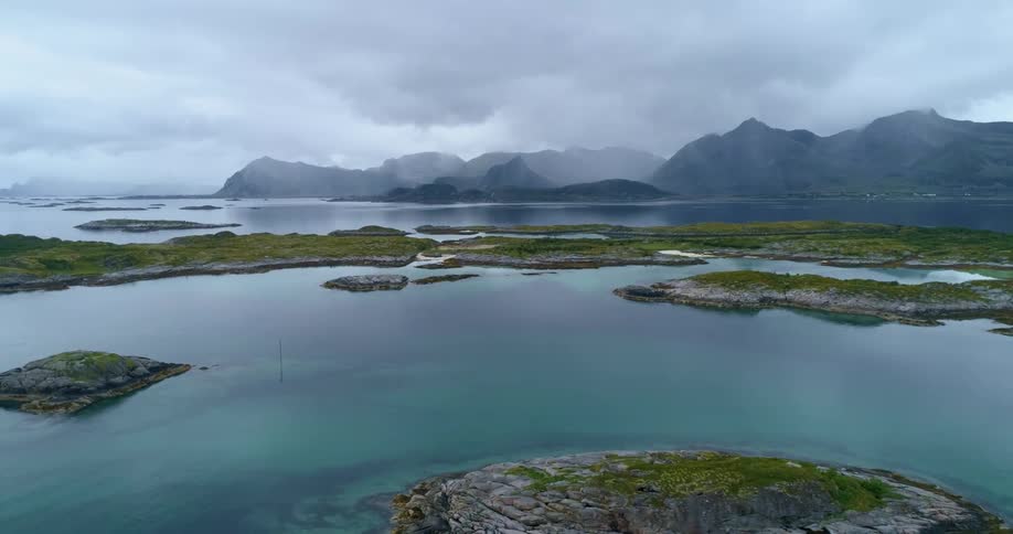 Islands of various sizes sit in water reflecting misty mountains and clouds