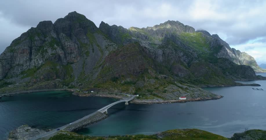 An aerial view of a body of water with a bridge and mountains with cloudy skies