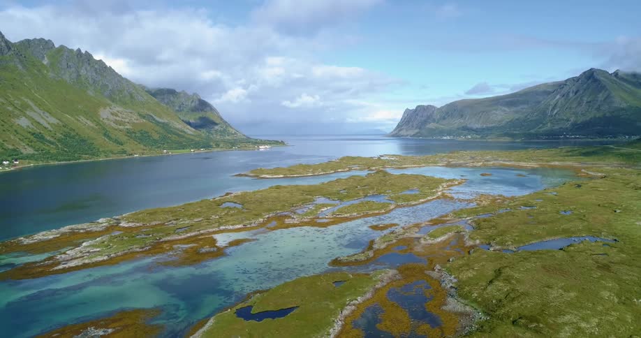 Blue water borders mountains and lowlands stretching to the horizon under a cloudy sky