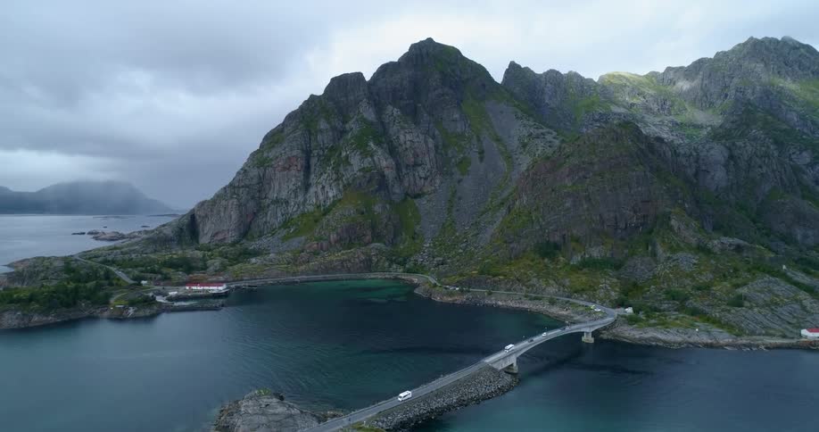 Cars drive down road and over bridge with the ocean cliffs and mountains around
