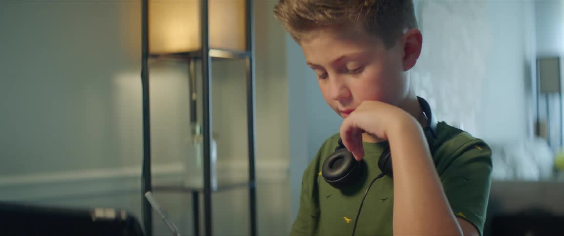 Boy with headphones and a green shirt sits at table and does homework in the living room at home