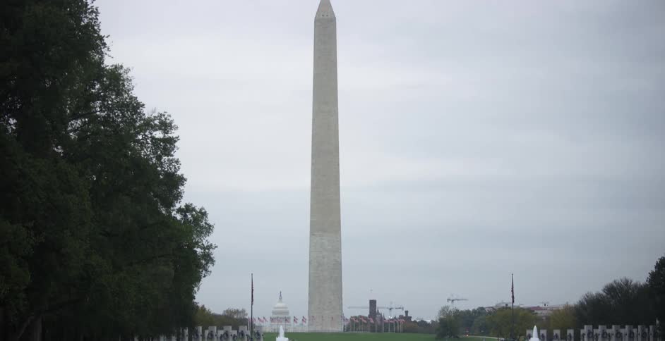 Washington monument at daytime with people walking by in the distance on a cloudy day