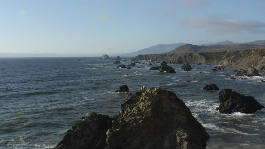 An aerial view of ocean coastline and mountains against a blue sky
