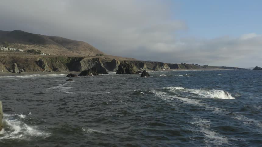 Waves crash into rocks along the coastline on a cloudy day
