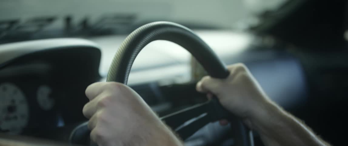 The hands of a man reach forward to grab a steering wheel inside of a car