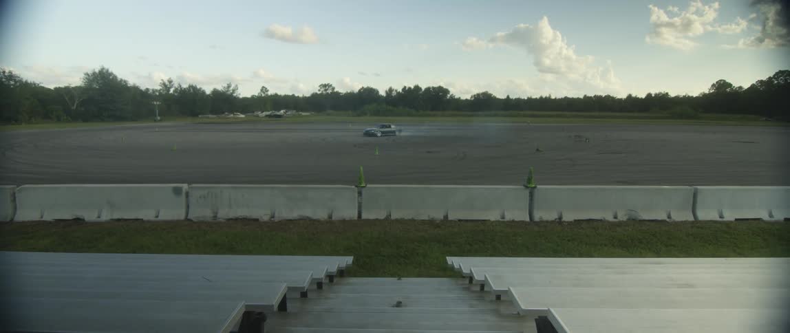 A car does donuts in a large open dirt race track area