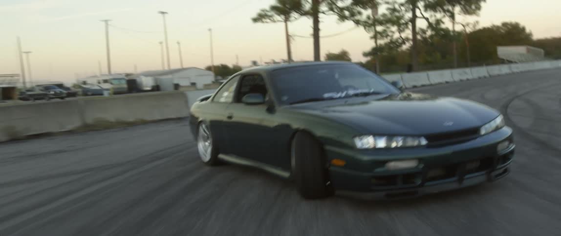 Green sports car drifting on an asphalt track next to a grass field during the day