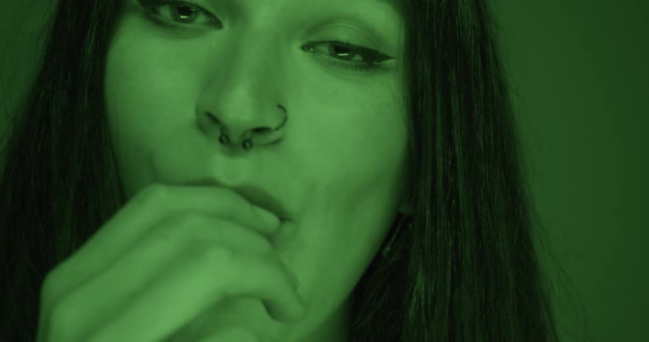 A model with long dark hair a nose ring winks as she holds her hand up to her mouth