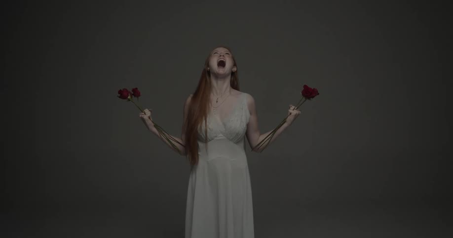 A red haired woman in a gown holds red roses in her hands as she screams