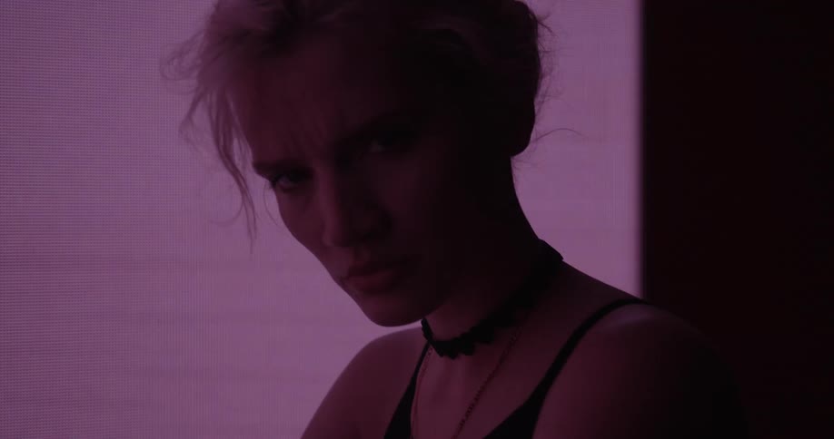Young blonde woman looking at the camera in front of a colorful digital display
