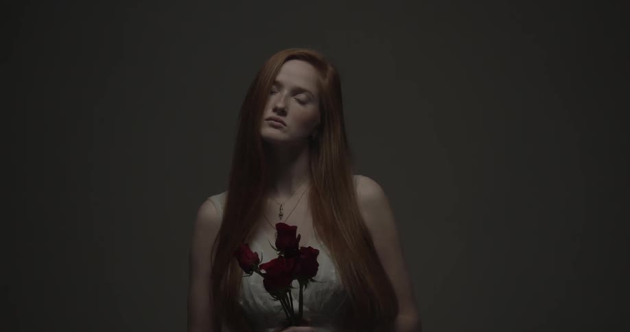 A woman tilts her head to the side while posing with dark red roses