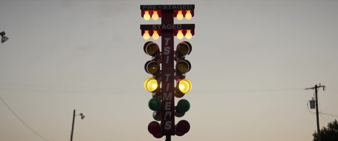 A drag race stoplight with a tree a utility pole the sky and clouds in the background