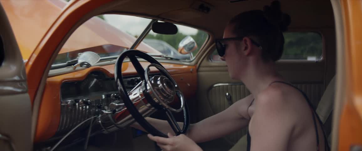 A woman sits in a classic car while touching the dashboard