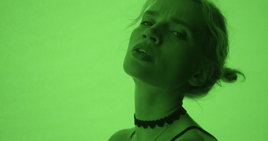 Woman sitting in front of a screen where the colors keep shifting while posing and staring at the camera