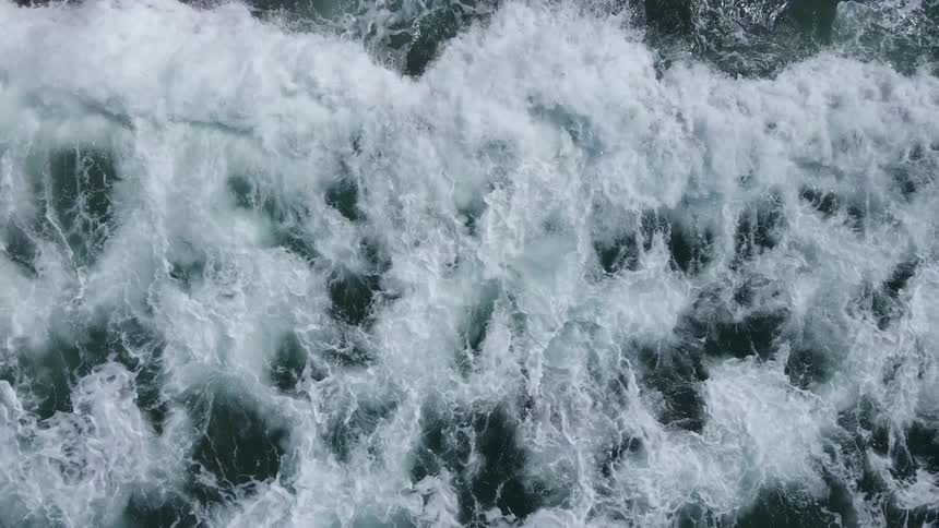 Aerial view of ocean waves crashing against the rocky shore