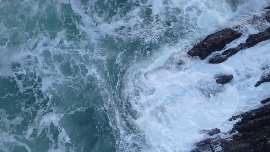 Aerial view of ocean waves crashing over the rocks on the coast