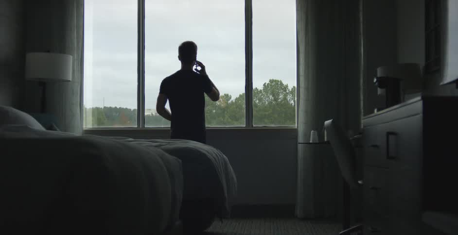 Silhouette of a man using a smartphone in front of a window in a bedroom