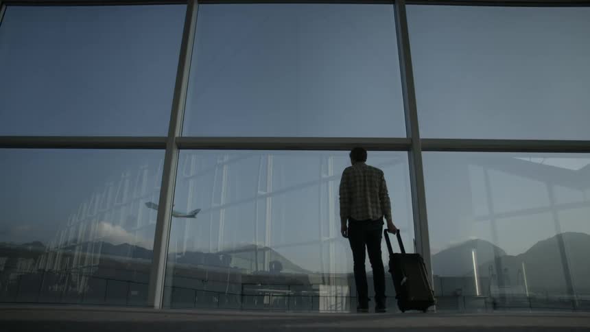People with luggage walk and stand by a window