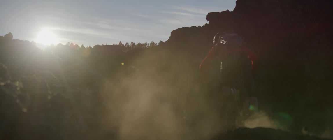Cyclist wearing a helmet and workout gear cycling on a dirt path on a mountain bike at sunrise