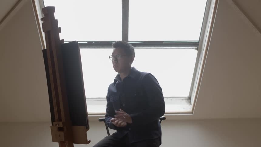 A man sitting down before an easel